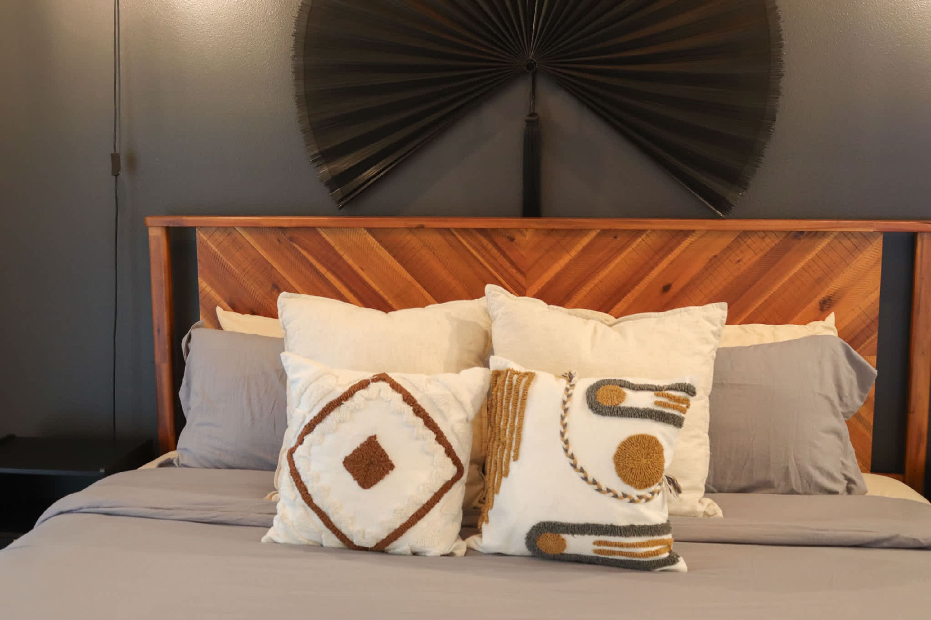 A bed with a wooden headboard, multiple pillows, and a wall-mounted fan.