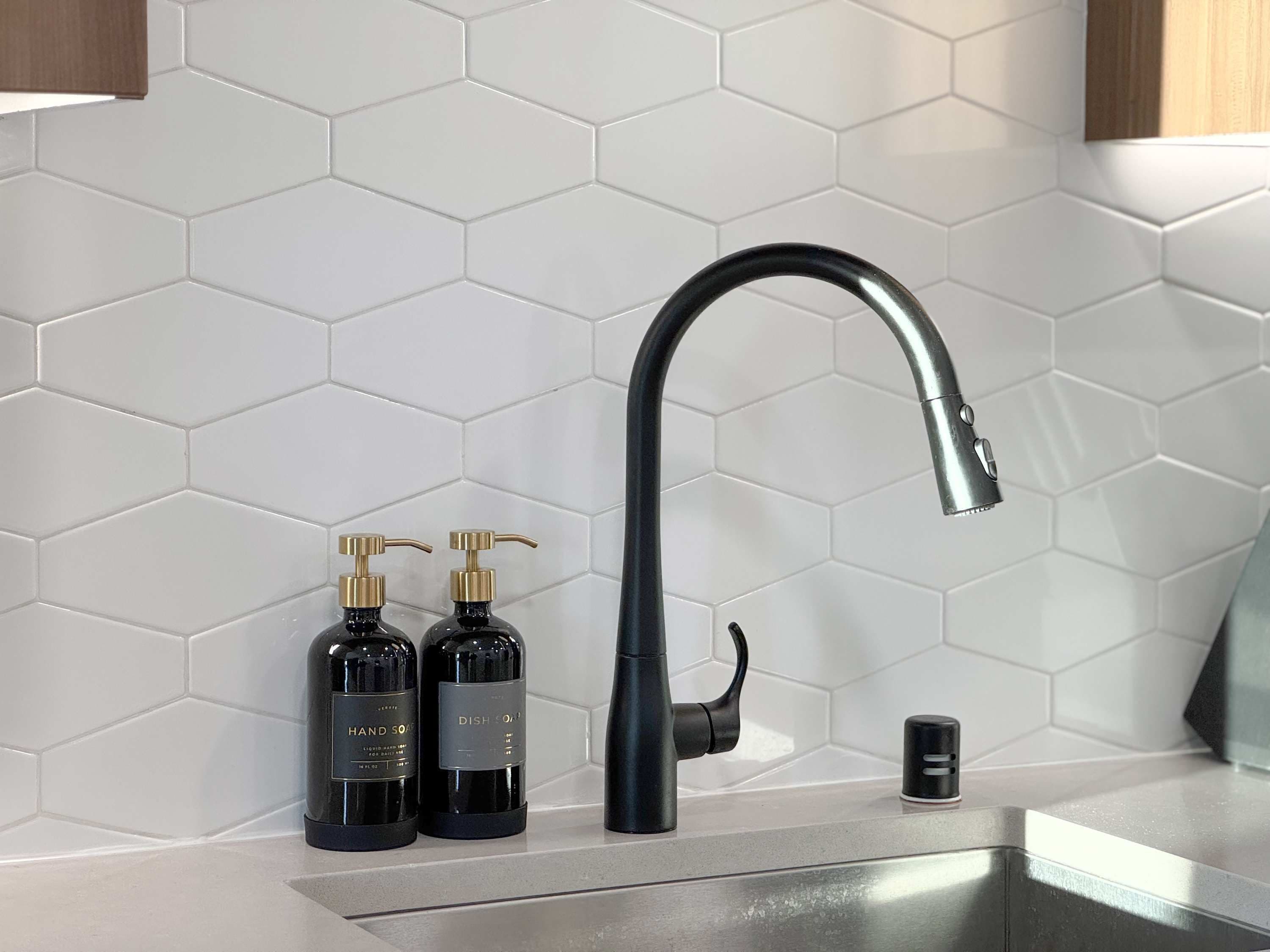 A kitchen with a modern black faucet, two black hand soap bottles, and a small black container on the counter.