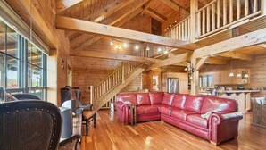 Un salón espacioso con un sofá seccional de cuero rojo, piso de madera y una escalera que sube a un nivel superior.