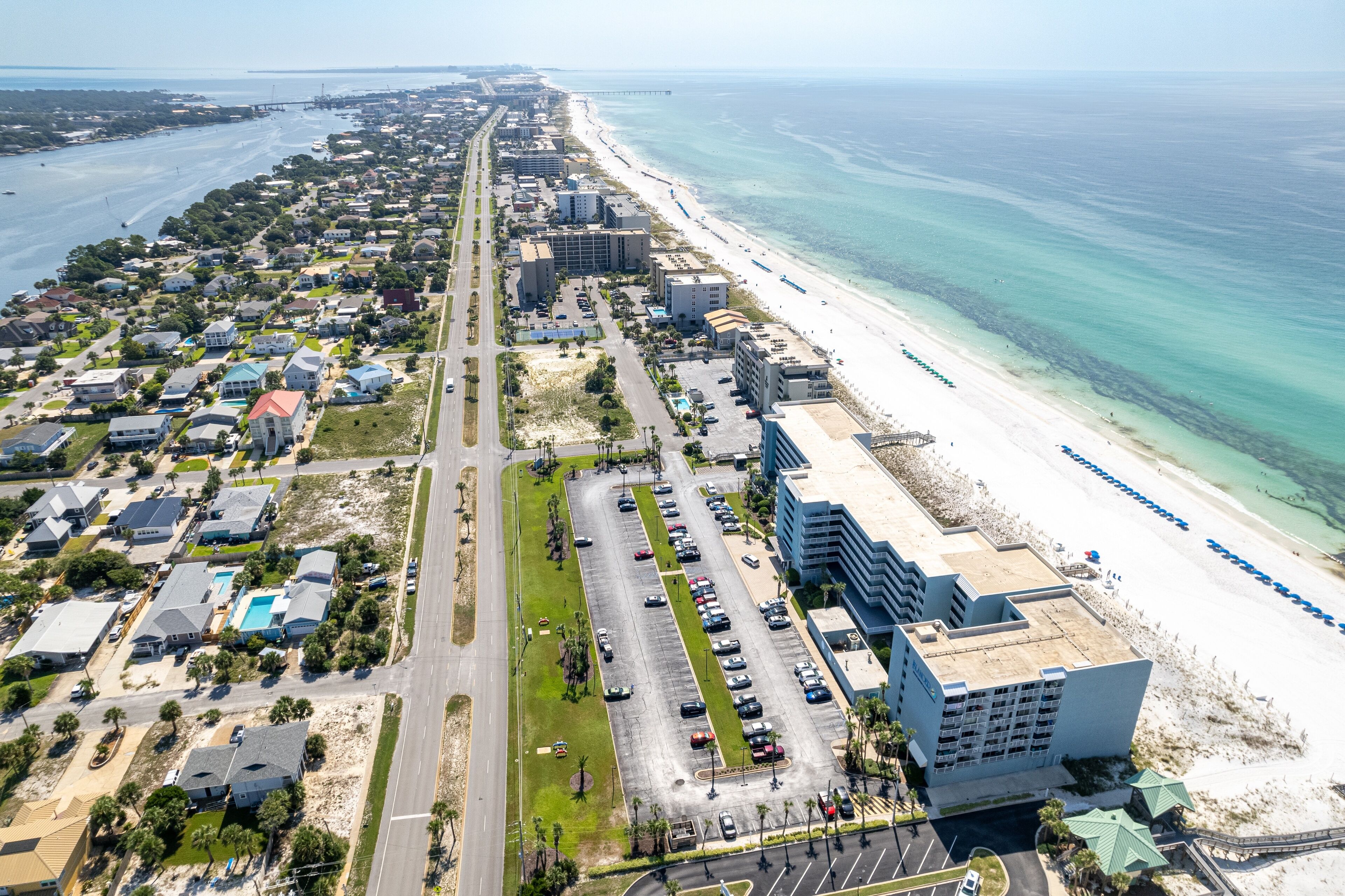 An aerial view of a coastal area with a beachfront hotel, a long road parallel to the beach, and residential buildings.