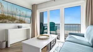 Una sala de estar moderna con un amplio ventanal con vistas a la playa, una consola blanca, un sofá azul y un sillón verde.