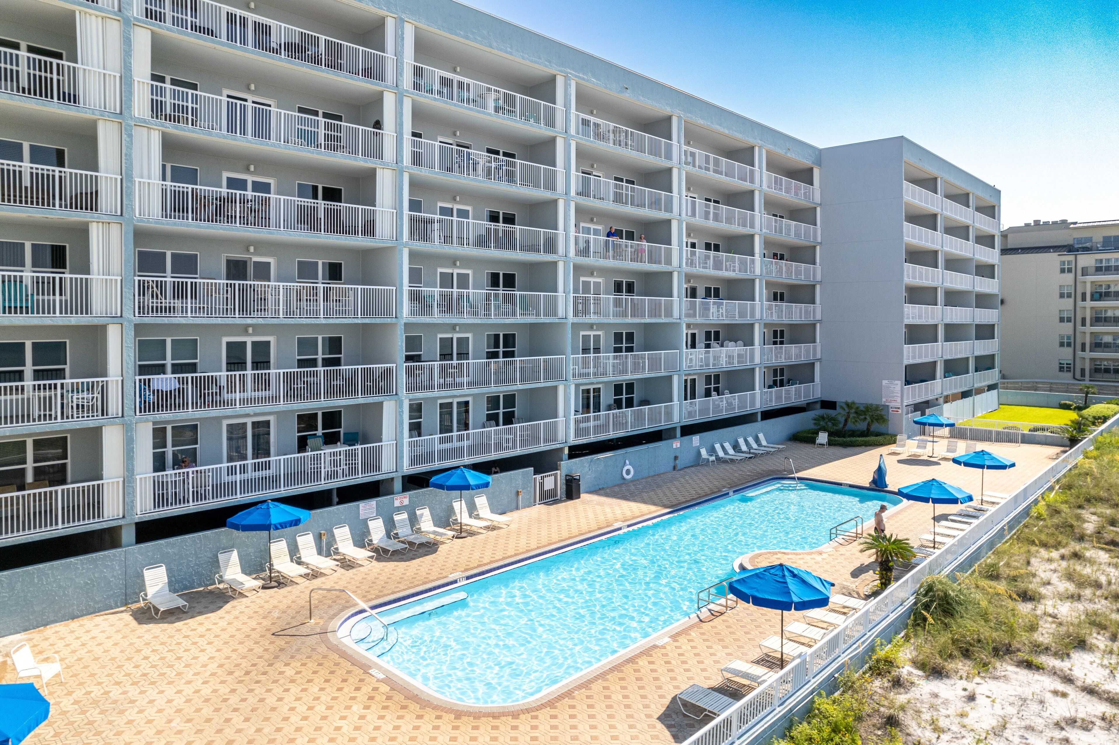 A multi-story hotel with a swimming pool, sun loungers, and umbrellas.