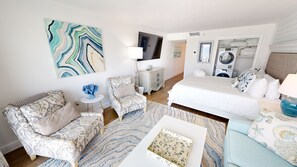 A hotel room with a bed, two armchairs, a small table, a mirror, a washing machine, and a large abstract painting. - Islander Beach Resort 403 Condo (Fort Walton Beach)