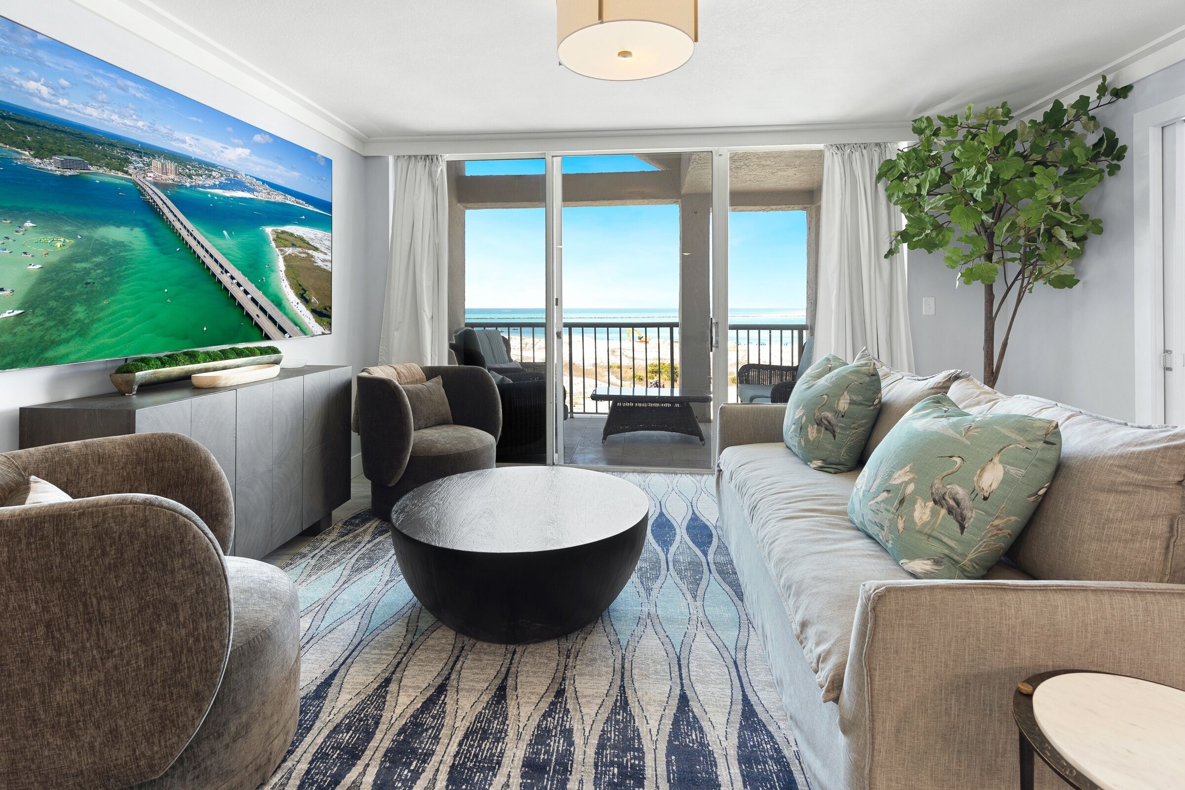 Un salon moderne doté d’un grand téléviseur, de sièges confortables, d’un balcon avec vue sur l’océan et d’une grande fenêtre.