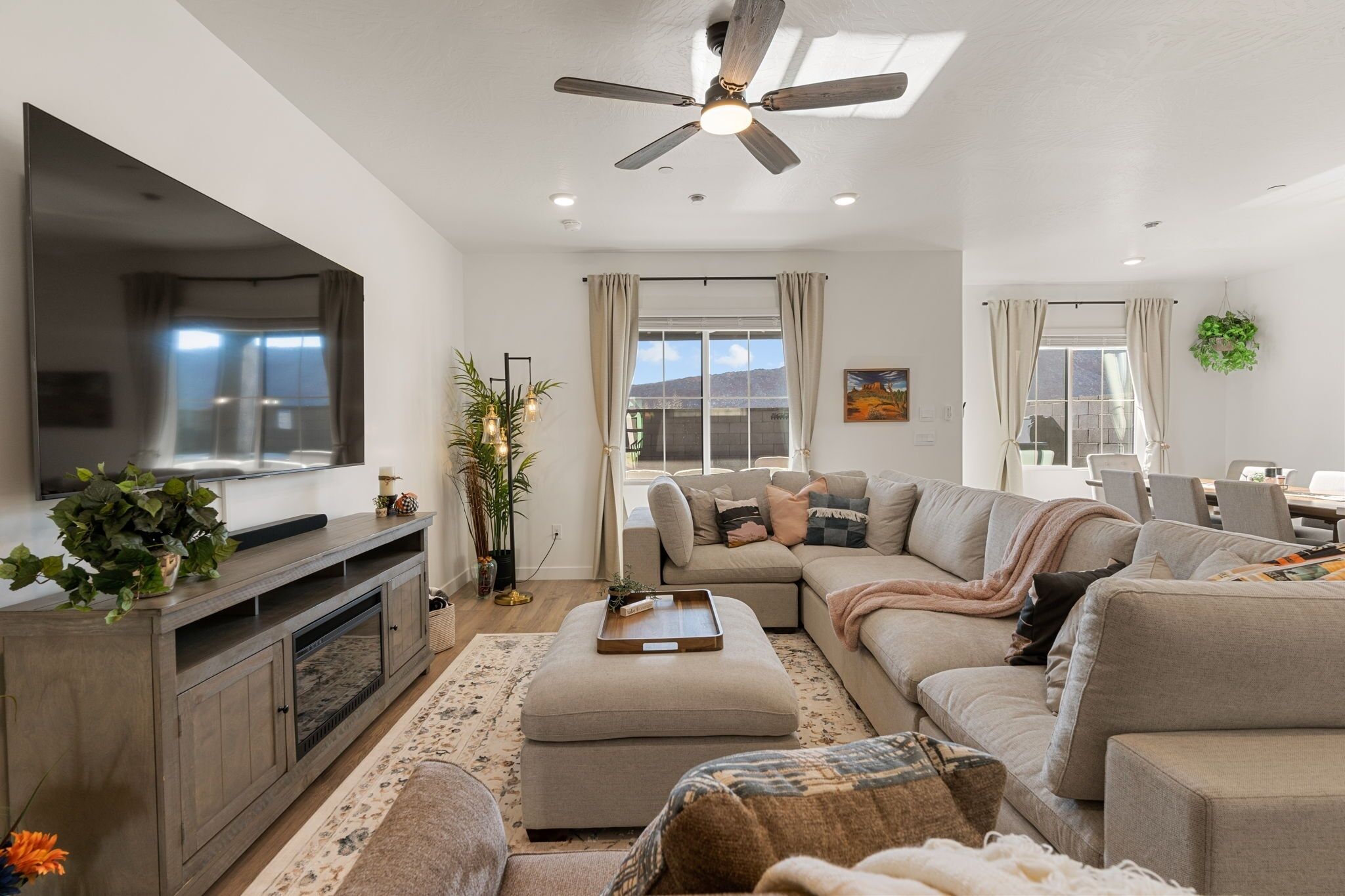 A modern living room with a large flat-screen TV, a ceiling fan, and a sofa set.