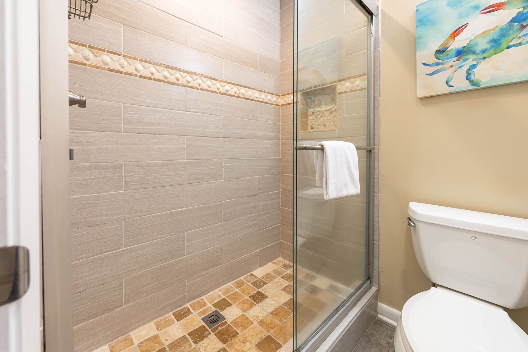 A bathroom with a glass shower enclosure, a white toilet, and a tiled floor with a decorative border.