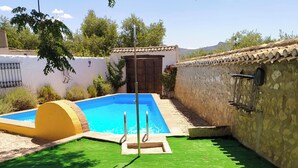 Une piscine avec une porte en bois, un foyer en pierre et deux chaises longues blanches.