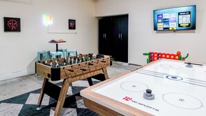 A room with a foosball table, a table tennis table, and a TV mounted on the wall displaying various streaming services.