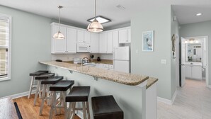 A modern kitchen with white cabinets, a granite countertop, and bar stools. - Walk to Beach 4BR Home with Pool Near Pier (Surfside Beach)