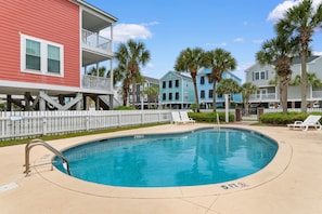 A swimming pool with a 5 FT depth marker, surrounded by a white fence, with multi-story buildings in the background.
