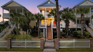 A two-story beachfront property with a central staircase, white picket fence, and palm trees. - Walk to Beach 4BR Home with Pool Near Pier (Surfside Beach)