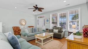 A spacious living room with a ceiling fan, a large window with blinds, and a wooden coffee table. - Walk to Beach 4BR Home with Pool Near Pier (Surfside Beach)