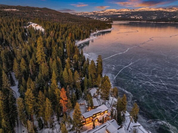 A lodge surrounded by dense forest and a frozen lake.