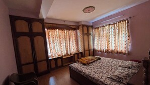 A bedroom with a bed, two windows with curtains, a wooden bench, and a ceiling light fixture.