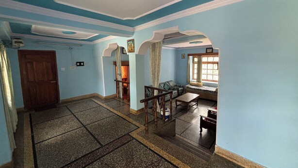 A spacious living room with a tiled floor, a wooden door, and a window with curtains.