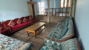 A spacious living room with a red sofa, a patterned sofa, and a wooden coffee table. There is a staircase leading to another room.