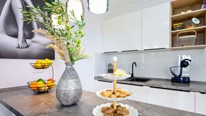 A modern kitchen with a marble countertop, a vase with green plants, a fruit bowl, a three-tiered serving tray with cookies, and a sink. - 2-Bedroom Holiday Villa Noa (Orebić)