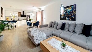 A modern living room with a grey sofa, a dining area with blue chairs, and a kitchen in the background. - 2-Bedroom Holiday Villa Noa (Orebić)