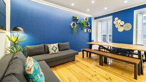 A modern living room with a blue accent wall, a grey sofa, a wooden dining table, and a bench.
