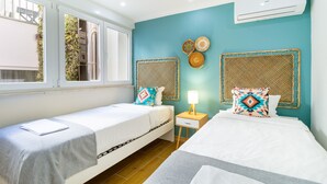 A twin bedroom with two beds, a window, a nightstand, and a wall-mounted air conditioner.