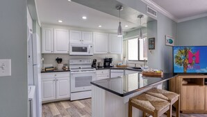 Una cocina moderna con armarios blancos, microondas integrado, estufa y una isla grande con encimera negra.