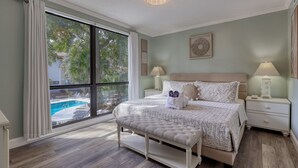 Un dormitorio con un ventanal grande, una cama con un banco y una mesita de noche con una lámpara.