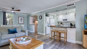 Sala de estar con sofá, una mesa de centro y una cocina americana con microondas, refrigerador y taburetes de bar.