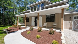 Une maison moderne à deux étages, dotée d’un porche abrité, d’une allée et d’un jardin aménagé avec du paillis et de petits arbustes.