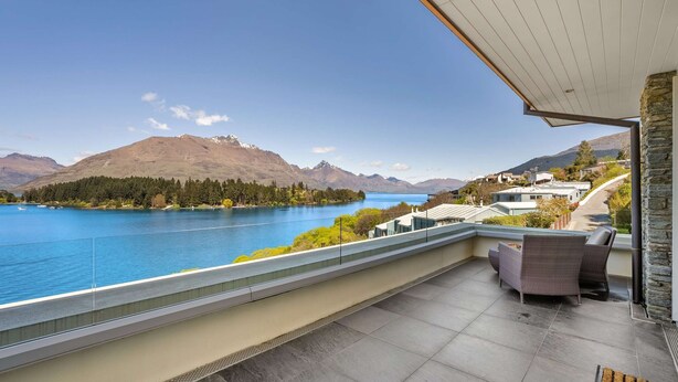 A balcony with a view of a lake, mountains, and a residential area.