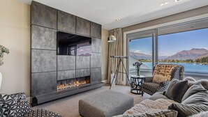 A modern living room with a fireplace, a sofa, and a view of a lake and mountains.