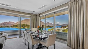 A dining room with a table set for six, large windows with curtains, and a view of mountains and a lake.