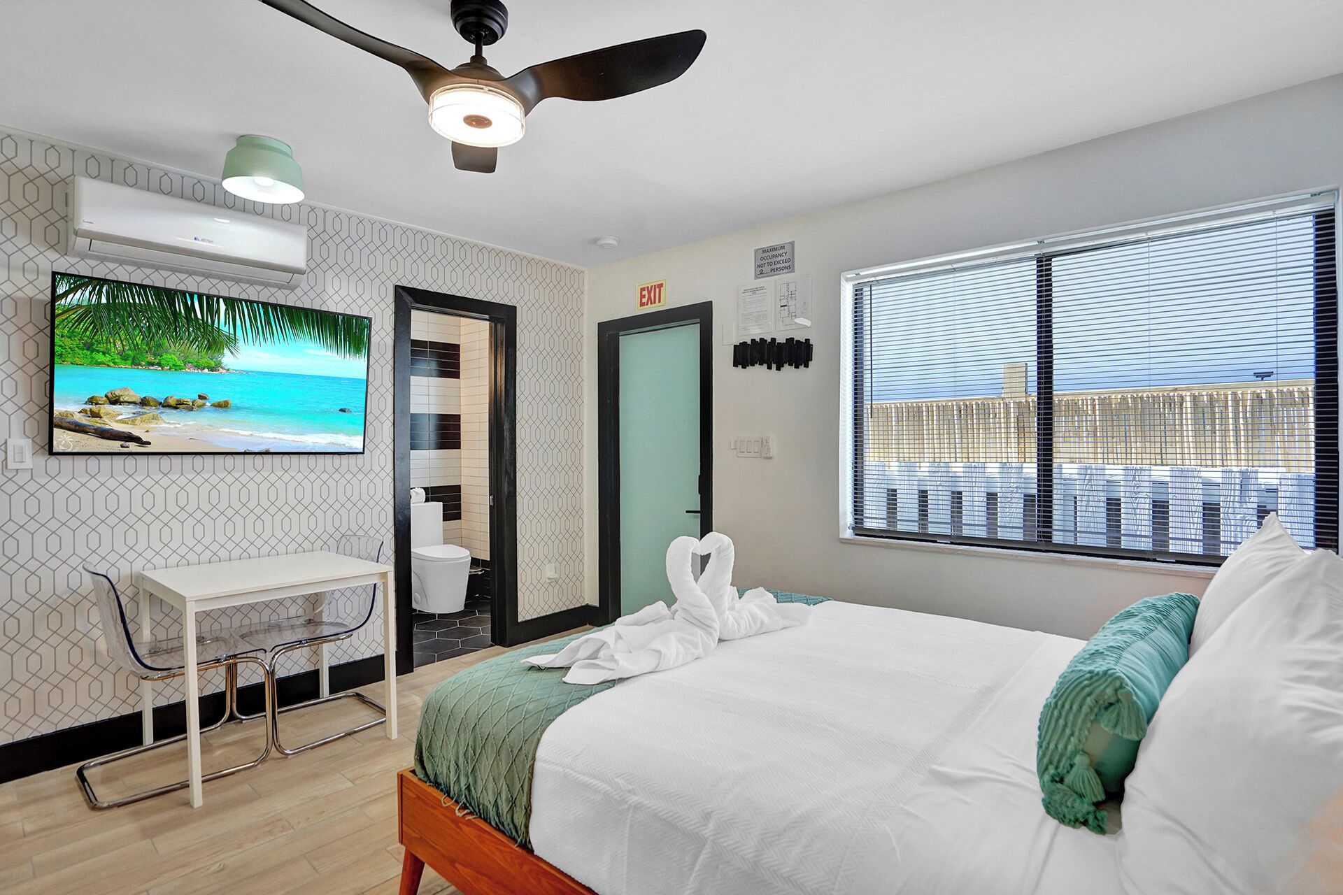 A hotel room with a bed, a desk, a chair, a TV, and a window with blinds.
