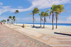 A beach with palm trees, a paved walkway, and the ocean in the background.