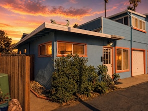 A two-story house with a blue exterior, a wooden fence, and a variety of plants.