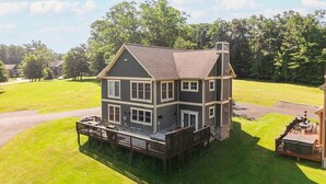 A two-story house with a deck, surrounded by a grassy yard and trees.