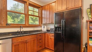 A kitchen with wooden cabinets, a black refrigerator, a window, and a dishwasher.