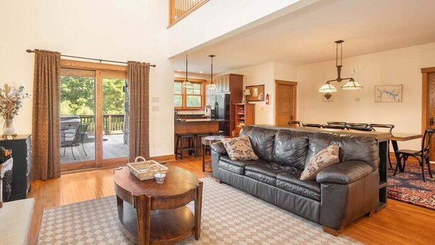 A spacious living room with a leather sofa, a dining table, and a kitchen in the background.