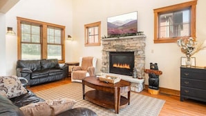 A living room with a stone fireplace, leather sofas, a coffee table, and a large window.
