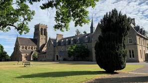 A historic building with a prominent tower, a large lawn, and a well-maintained garden. - Porters Lodge (Hereford)