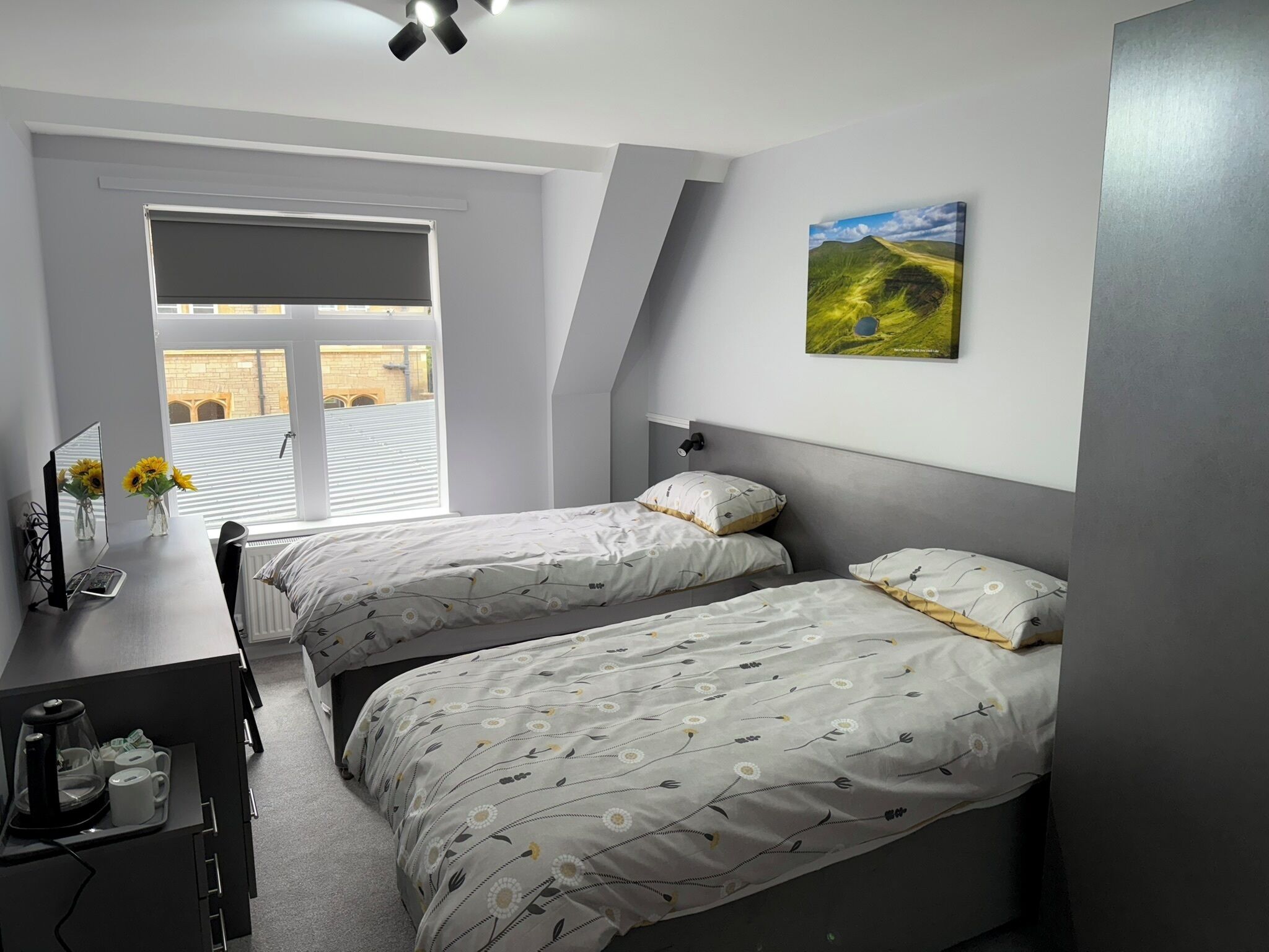 Een slaapkamer met twee bedden, een bureau en een raam met zonwering.