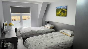Een slaapkamer met twee bedden, een bureau en een raam met zonwering.