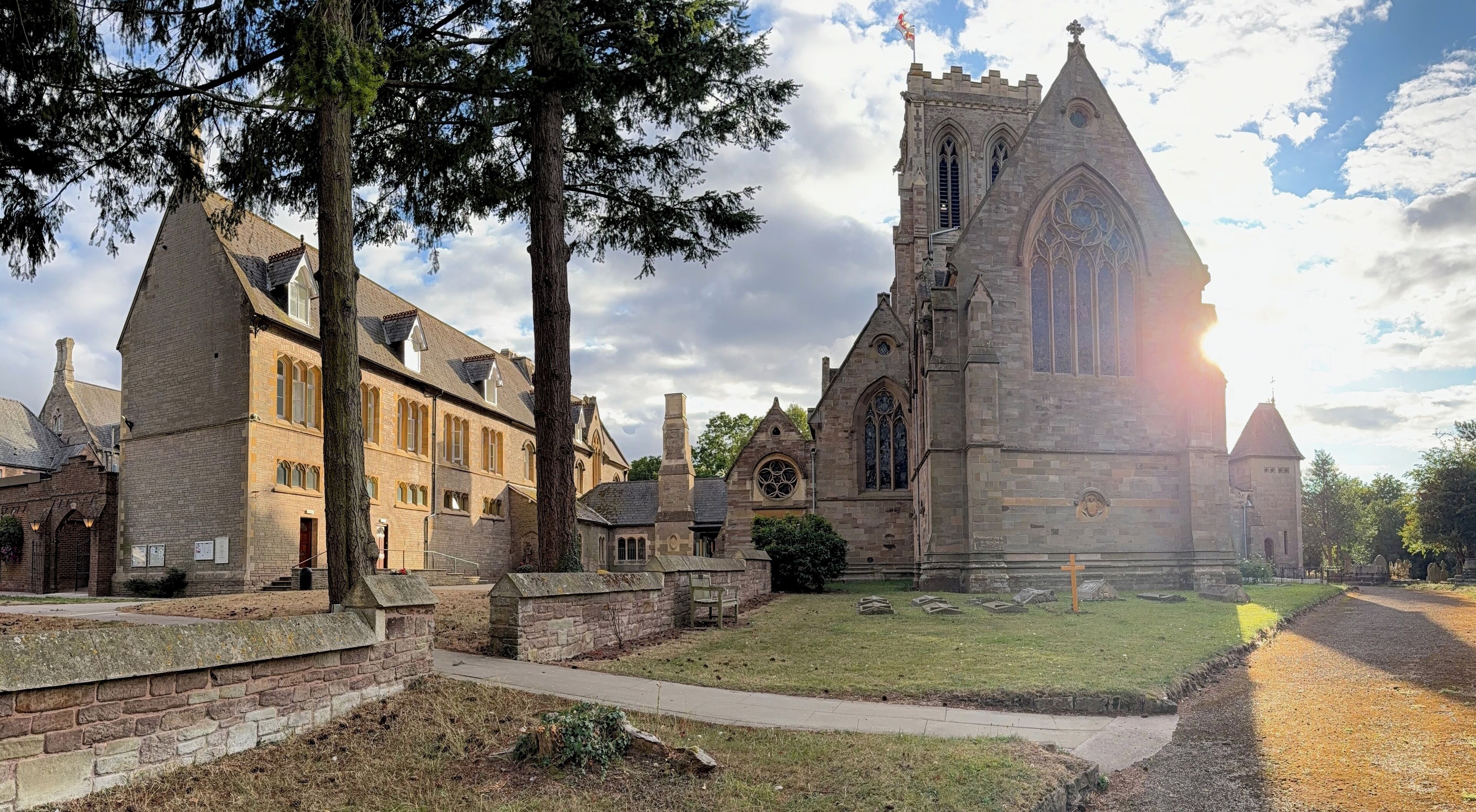 A historic church with a prominent tower and large windows, surrounded by stone buildings and a grassy area.