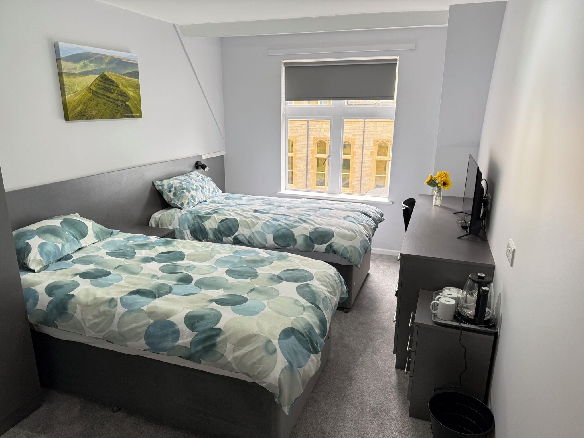 Una camera da letto con due letti, una scrivania, una sedia, una finestra e un quadro appeso al muro.
