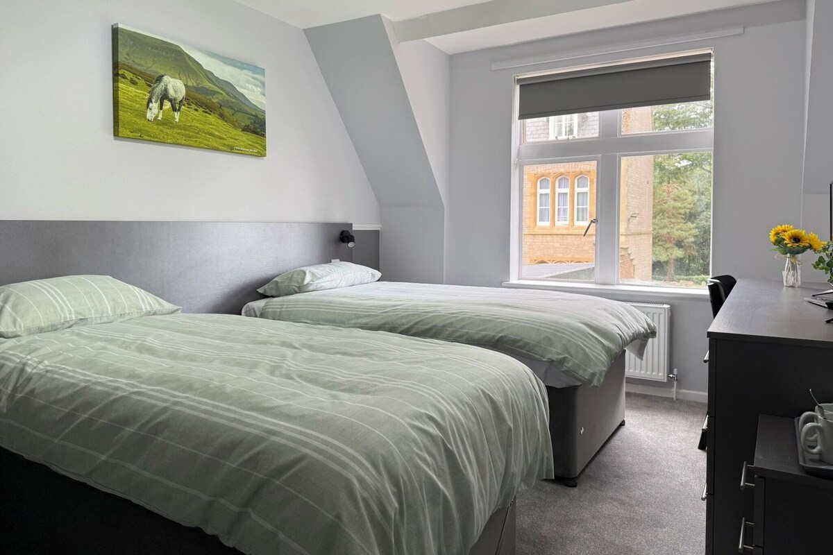 A bedroom with two beds, a window with a view of a building, and a painting of a horse on the wall.