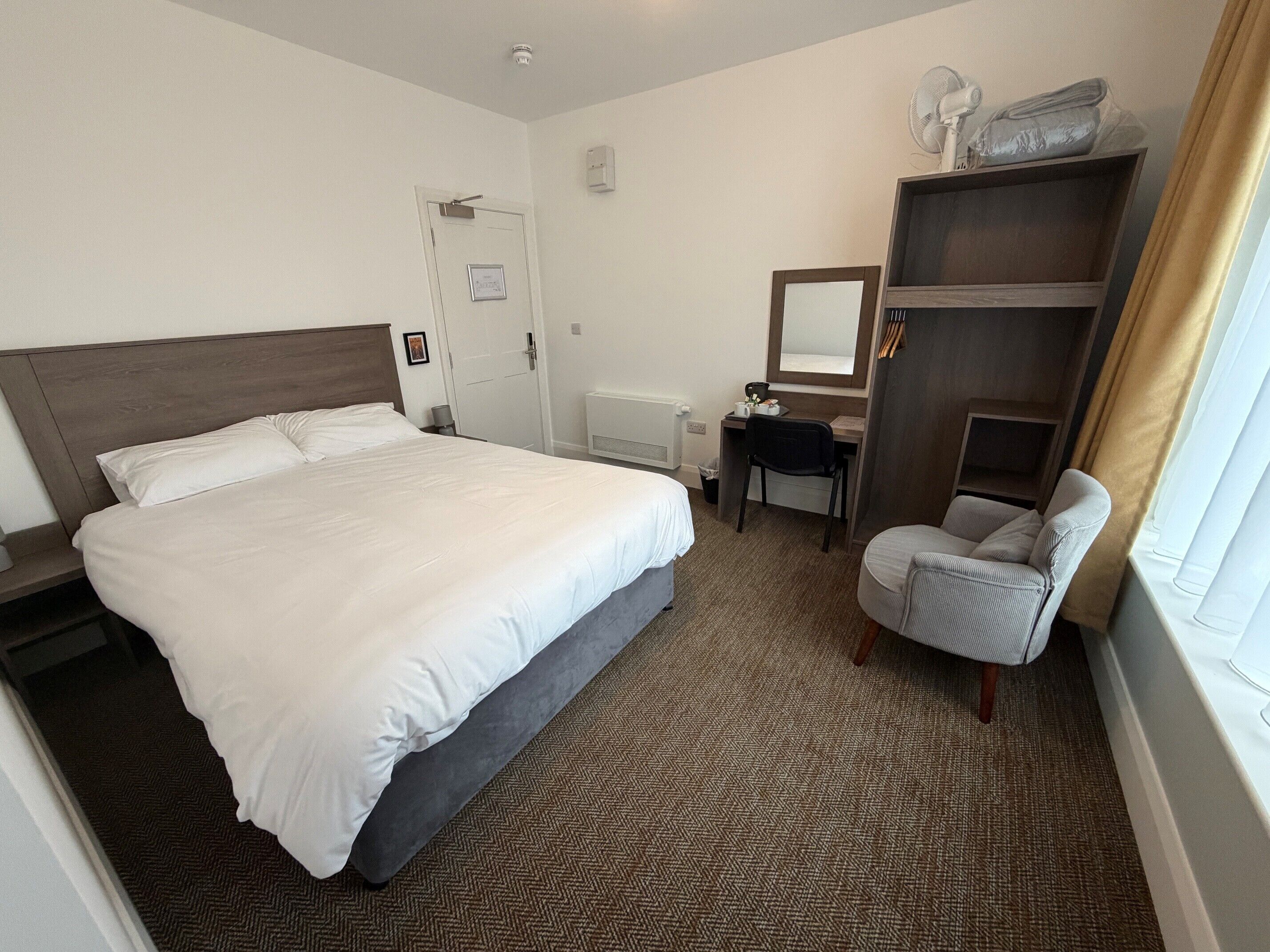 Una habitación de hotel con una cama grande, un escritorio, una silla, un armario y una ventana con cortinas.