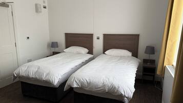 A hotel room with two single beds, bedside tables with lamps, a door, and a window with curtains.