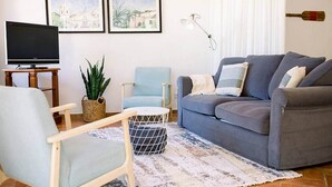 Un salon avec un canapé, un fauteuil, une télévision et une plante.