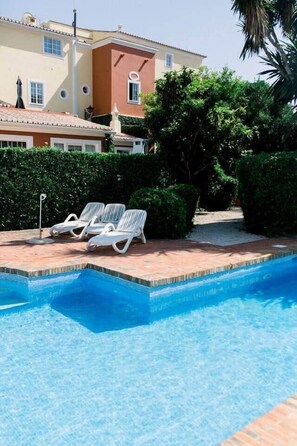 A swimming pool with lounge chairs, surrounded by a brick patio and greenery.
