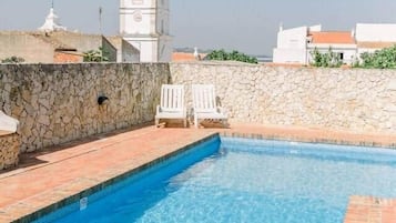 A swimming pool with a stone wall and a white tower in the background.