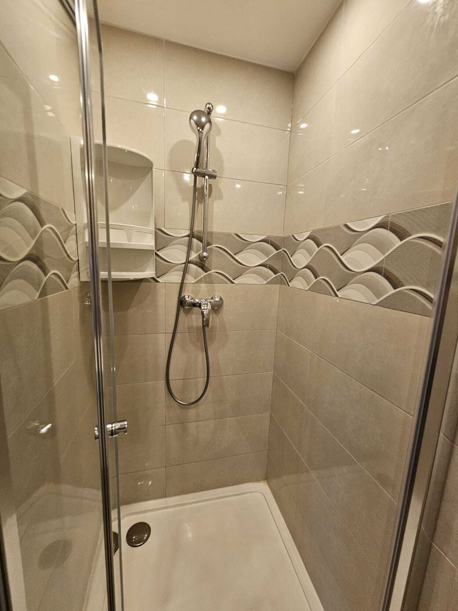 Eine Duschkabine mit Handbrause und am Wand montiertem Wasserhahn.